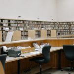 Interior view of a university library with bookshelves and computer workstations.